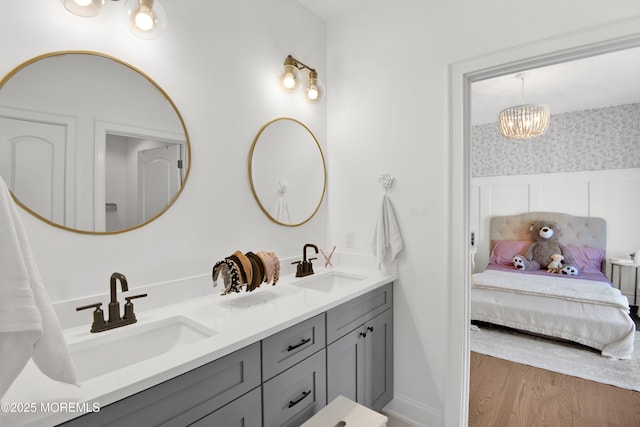 full bath featuring a sink, wood finished floors, double vanity, and wallpapered walls