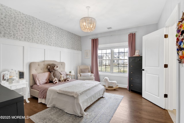 bedroom featuring a wainscoted wall, visible vents, dark wood-type flooring, wallpapered walls, and a chandelier