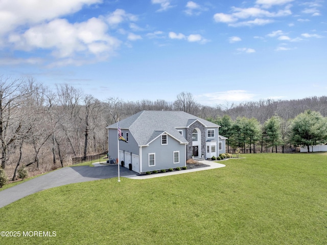 view of front of home featuring a forest view, driveway, an attached garage, and a front lawn