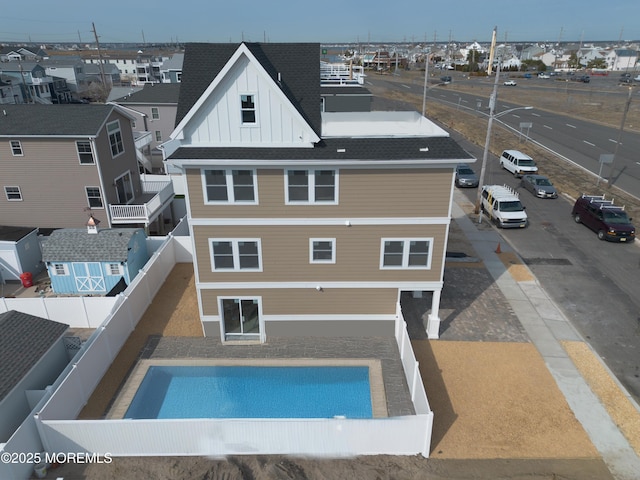 rear view of house with board and batten siding, a shingled roof, a residential view, a fenced backyard, and uncovered parking