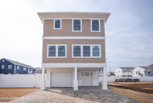 coastal inspired home with decorative driveway, a garage, and fence