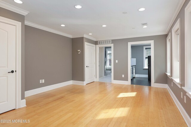 empty room featuring light wood-style flooring, recessed lighting, baseboards, visible vents, and ornamental molding