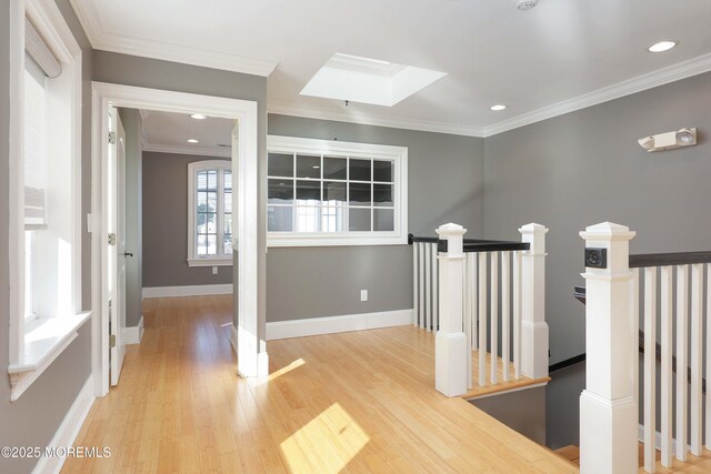 hall featuring light wood finished floors, baseboards, an upstairs landing, a skylight, and ornamental molding