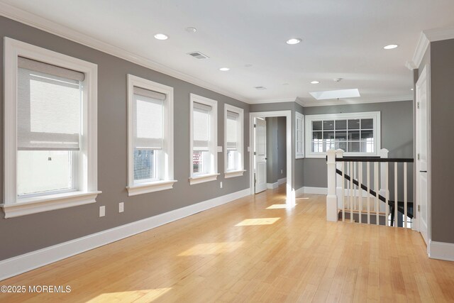 empty room featuring a skylight, baseboards, ornamental molding, and a healthy amount of sunlight