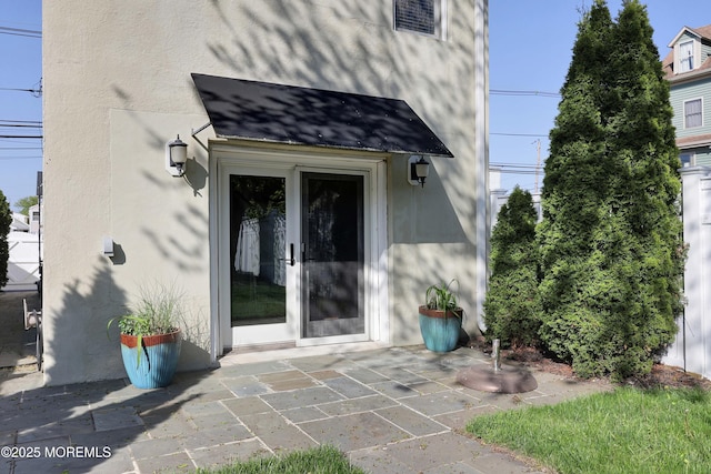 doorway to property featuring a patio, a shingled roof, and stucco siding