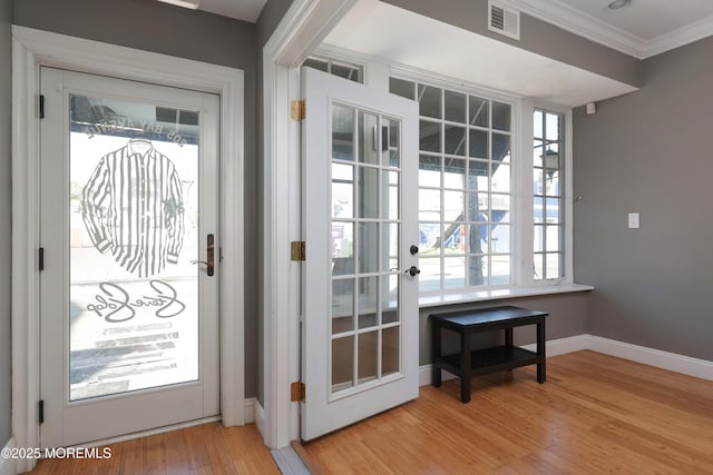 doorway to outside with a wealth of natural light, light wood-type flooring, visible vents, ornamental molding, and baseboards