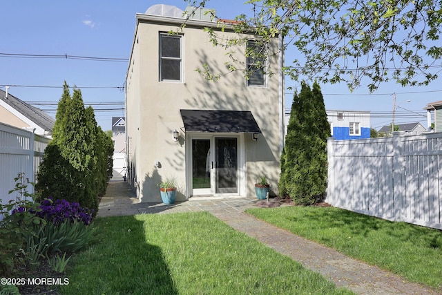 rear view of property featuring a lawn, fence, and stucco siding