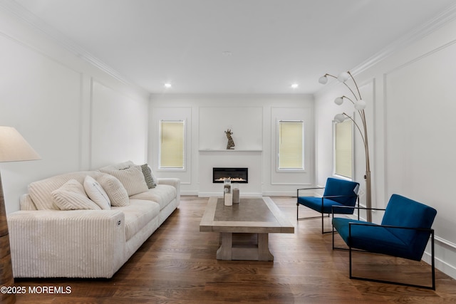 living room with dark wood-type flooring, a glass covered fireplace, crown molding, and a decorative wall