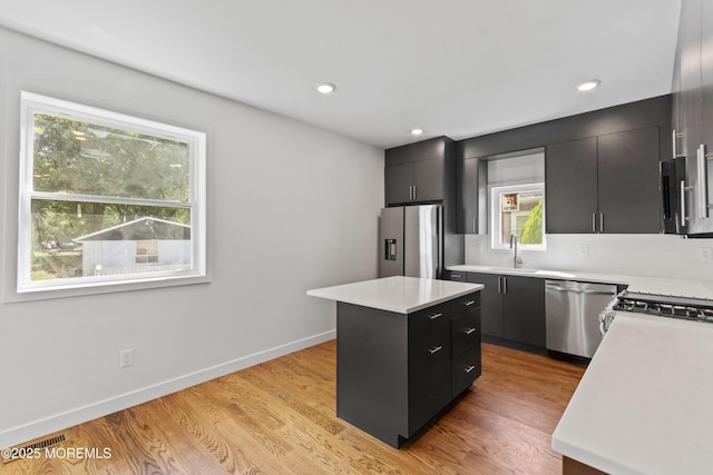 kitchen featuring a sink, a center island, appliances with stainless steel finishes, light wood finished floors, and dark cabinets