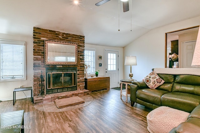 living room featuring a ceiling fan, wood finished floors, baseboards, a brick fireplace, and vaulted ceiling