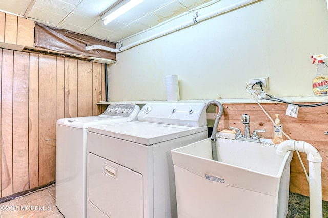 laundry area featuring wooden walls, light tile patterned floors, laundry area, washer and dryer, and a sink