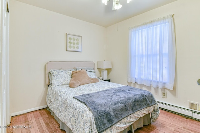 bedroom featuring a baseboard heating unit, multiple windows, wood finished floors, and baseboards