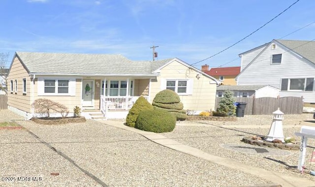 bungalow-style home featuring fence, covered porch, and roof with shingles