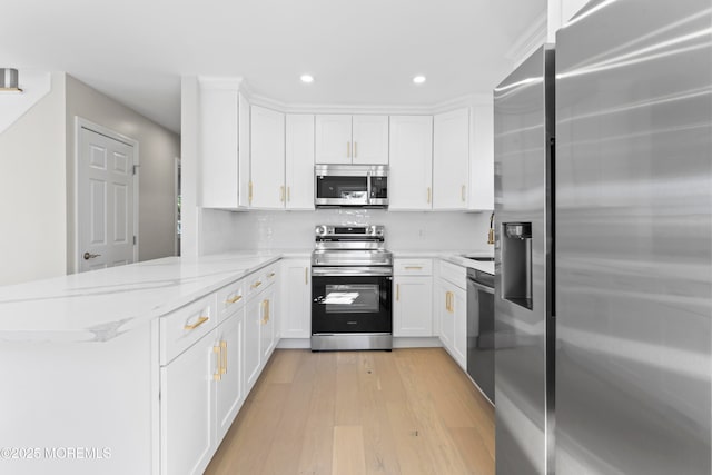 kitchen featuring light wood-style flooring, stainless steel appliances, a peninsula, white cabinets, and light stone countertops