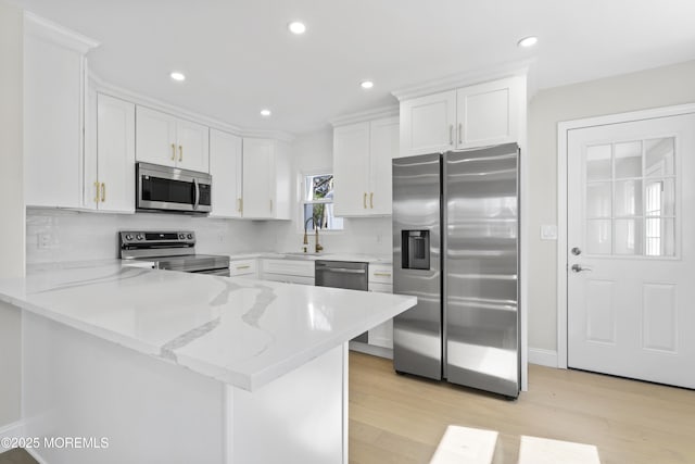 kitchen featuring light wood finished floors, a peninsula, a sink, stainless steel appliances, and white cabinets