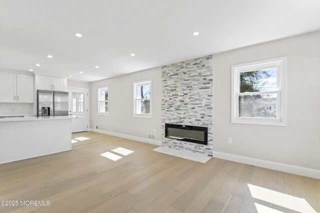 unfurnished living room featuring recessed lighting, light wood-type flooring, a large fireplace, and baseboards