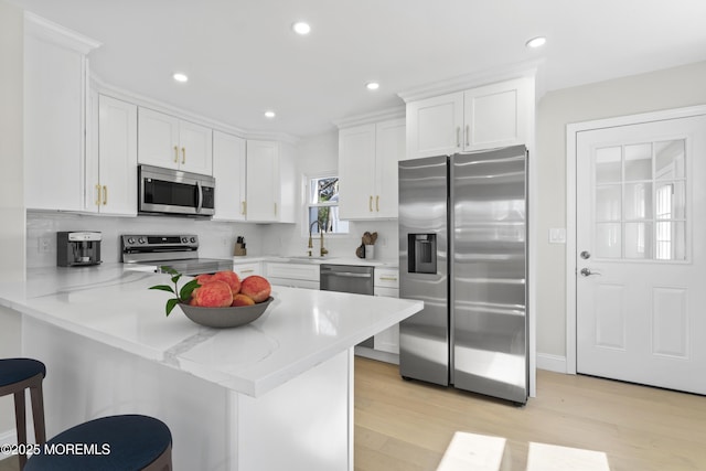 kitchen featuring light countertops, appliances with stainless steel finishes, a peninsula, white cabinetry, and a sink