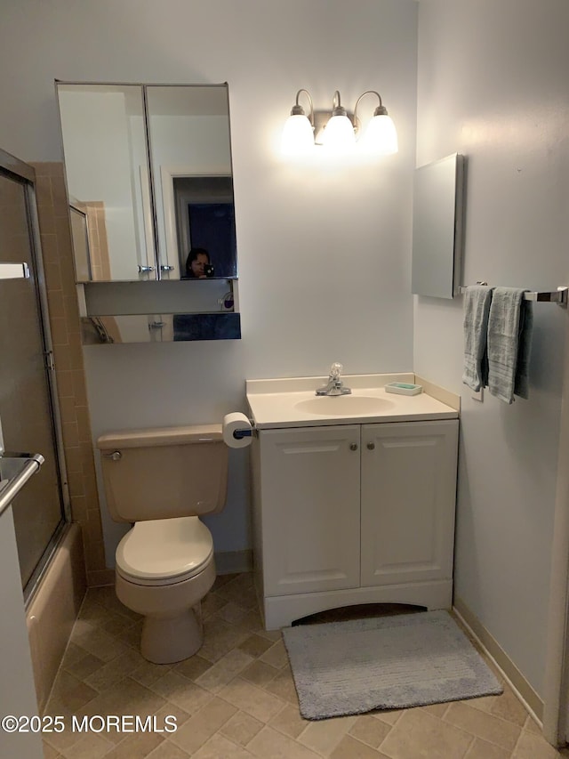 bathroom with combined bath / shower with glass door, toilet, vanity, and baseboards