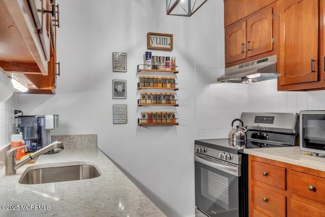 kitchen with brown cabinets, under cabinet range hood, a sink, appliances with stainless steel finishes, and decorative backsplash