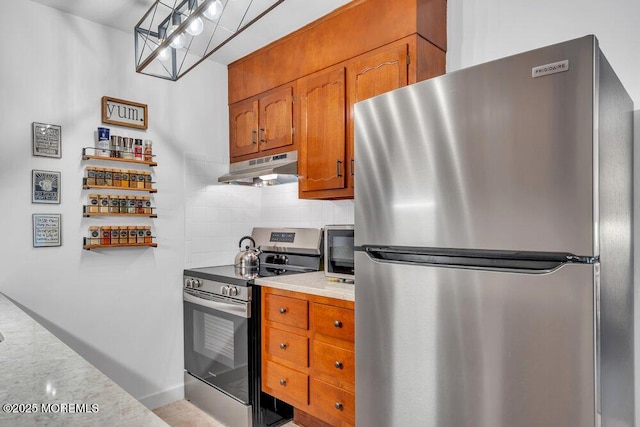 kitchen with brown cabinets, under cabinet range hood, stainless steel appliances, light countertops, and decorative backsplash