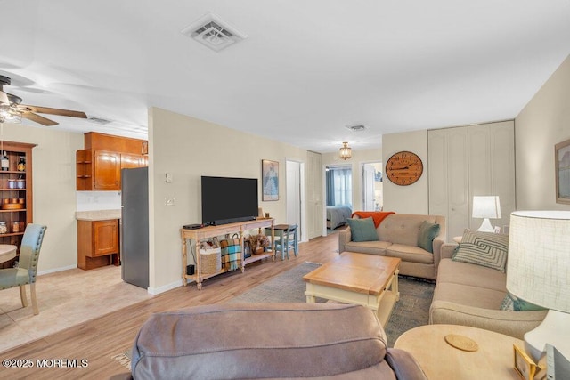 living room featuring visible vents, baseboards, ceiling fan, and light wood finished floors