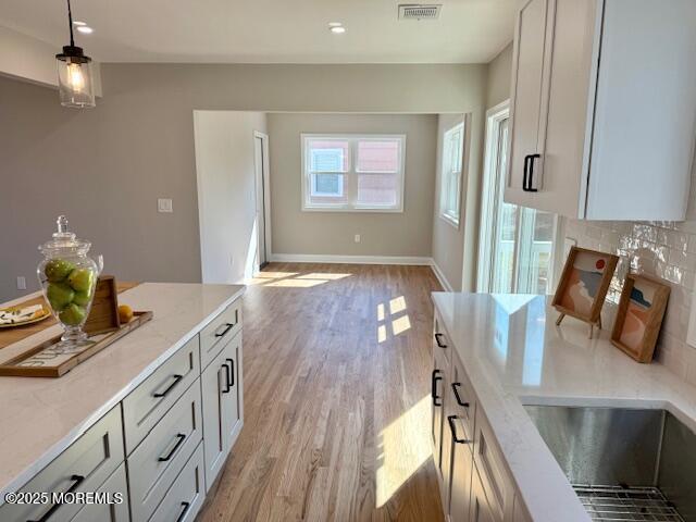 kitchen featuring light wood finished floors, visible vents, baseboards, light stone countertops, and hanging light fixtures