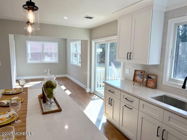 kitchen featuring white cabinetry, light wood-style flooring, decorative light fixtures, and a sink