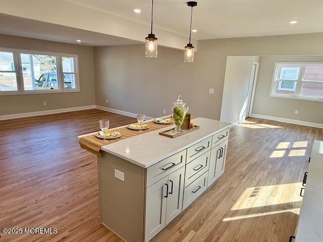 kitchen with baseboards, light wood-style floors, decorative light fixtures, open floor plan, and a center island