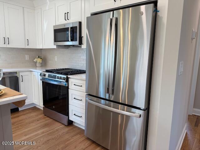 kitchen featuring light wood finished floors, appliances with stainless steel finishes, white cabinetry, and light countertops