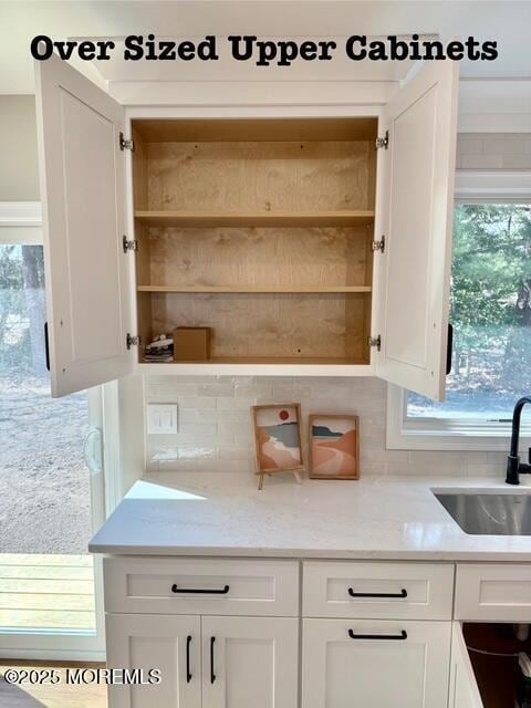 interior space featuring open shelves, a sink, tasteful backsplash, white cabinets, and light stone countertops