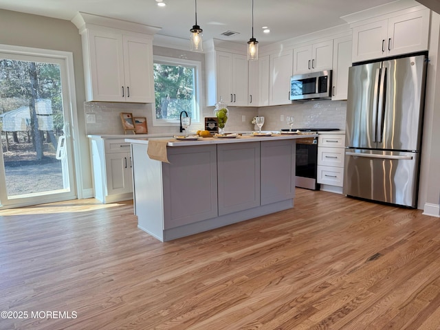 kitchen with a center island, light wood-type flooring, light countertops, appliances with stainless steel finishes, and white cabinets