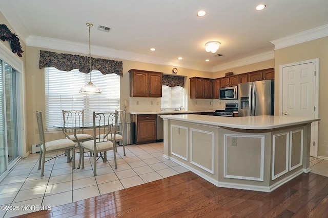 kitchen featuring light countertops, light wood-style floors, appliances with stainless steel finishes, and ornamental molding