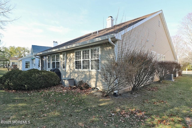 view of side of home with cooling unit, a lawn, and a chimney