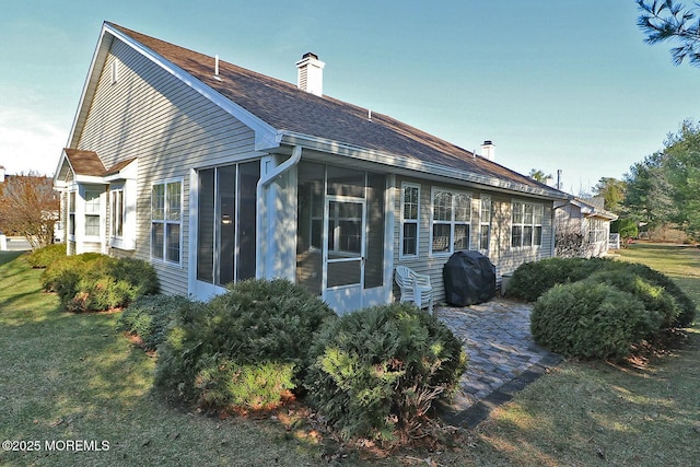 back of property with roof with shingles, a yard, a sunroom, and a chimney
