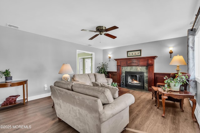 living room featuring visible vents, ceiling fan, wainscoting, a fireplace, and wood finished floors