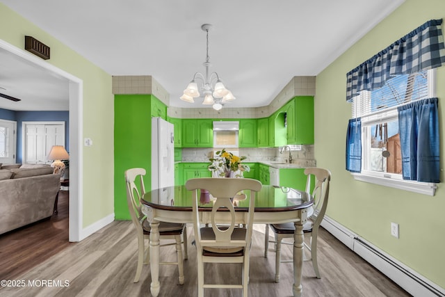 dining area with light wood-type flooring, a baseboard radiator, a notable chandelier, and a healthy amount of sunlight