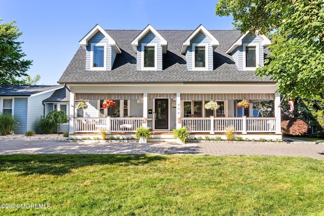 new england style home featuring covered porch, a front lawn, and roof with shingles