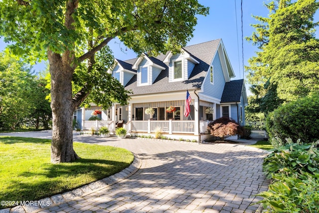 cape cod-style house featuring a porch, a front yard, and a shingled roof