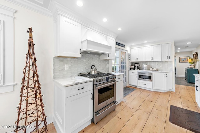 kitchen featuring premium range hood, light wood-type flooring, backsplash, appliances with stainless steel finishes, and white cabinets