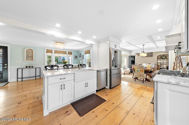 kitchen with light wood-style flooring, appliances with stainless steel finishes, a peninsula, white cabinets, and a sink