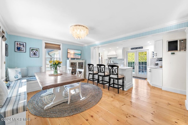 dining room featuring crown molding, decorative columns, french doors, light wood-style floors, and a notable chandelier