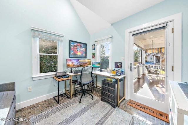 office space featuring brick floor, lofted ceiling, and baseboards