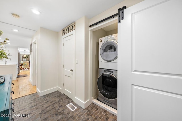 laundry room with baseboards, a barn door, laundry area, recessed lighting, and stacked washer / drying machine