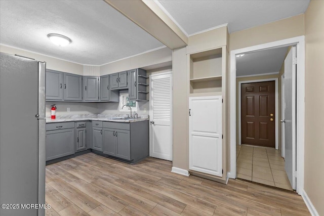 kitchen featuring a sink, gray cabinetry, light wood-style flooring, freestanding refrigerator, and open shelves