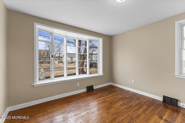 empty room featuring a wealth of natural light, visible vents, baseboards, and dark wood-style floors