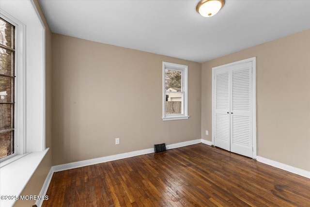 unfurnished bedroom featuring dark wood-style floors, a closet, and baseboards