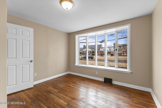 spare room with visible vents, baseboards, and dark wood-style flooring