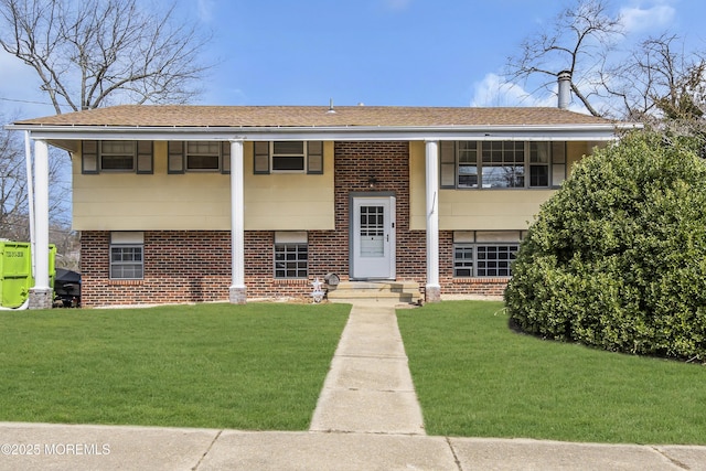 raised ranch featuring brick siding, a shingled roof, and a front yard