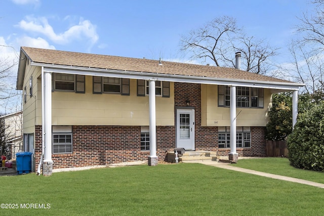 view of front of home with brick siding, a front yard, and roof with shingles