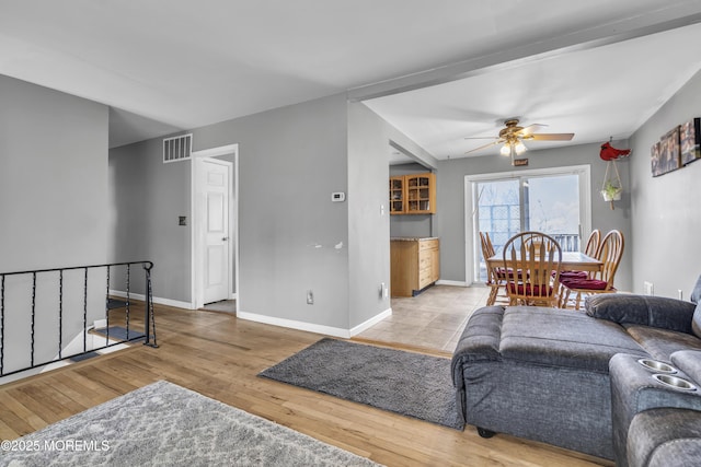 living area featuring visible vents, baseboards, ceiling fan, and light wood finished floors